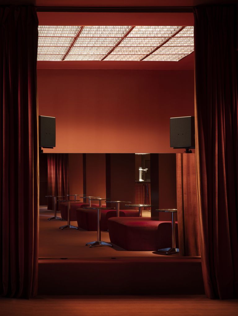 A modern caf&eacute; with warm, inviting tones, featuring rich red hues on the walls and furniture, and a glass ceiling that adds a contemporary touch to the lighting