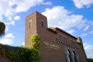 Facade of The Borgata in Scottsdale, featuring a traditional Tuscan design with arched windows and decorative details, with a golden sign displaying the center's name.