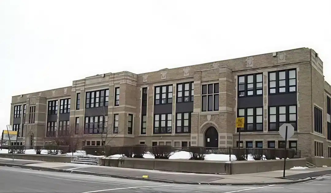 A historic building with a traditional architectural design, shown from the outside with large windows and a prominent main entrance. The building is constructed of yellow brick and surrounded by some trees and green spaces.