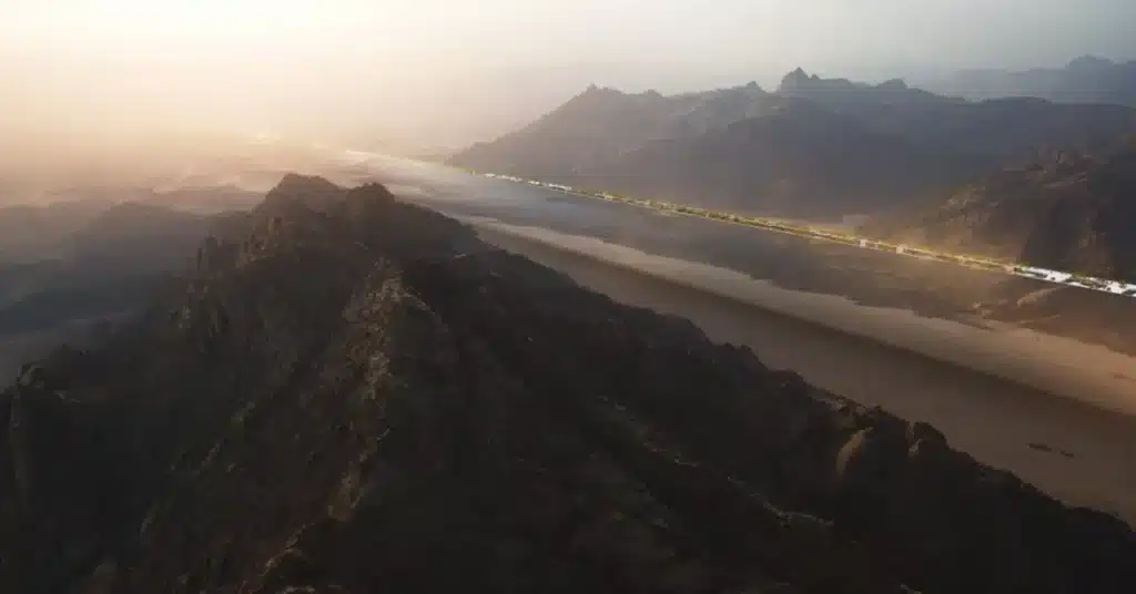 A breathtaking natural landscape featuring towering mountains, a river flowing through a valley, and a modern city in the distance.