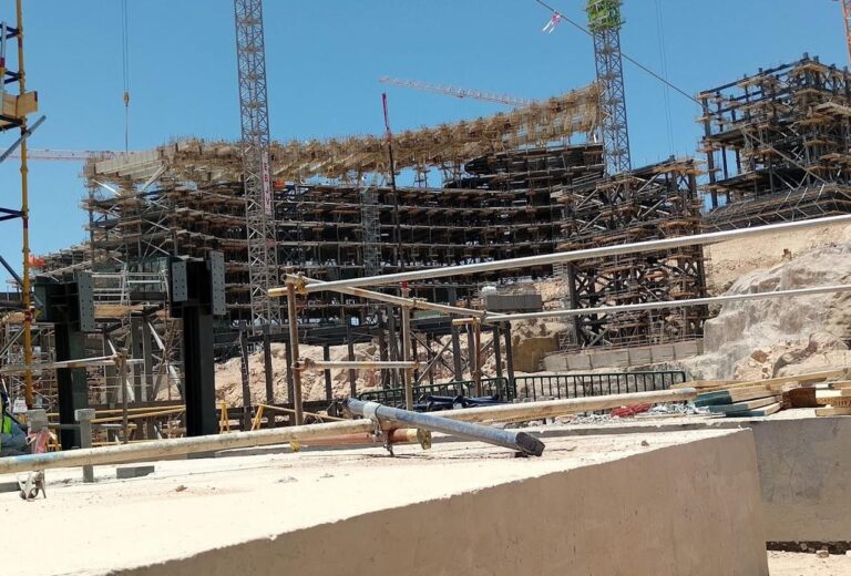 Construction activities showcase metal and wooden frameworks in the Trojina Mountain Project, with support columns and structural reinforcements being installed. Caption (English): "The Trojina Mountain Project is making significant progress as metallic and wooden structures rise amidst rugged terrain.