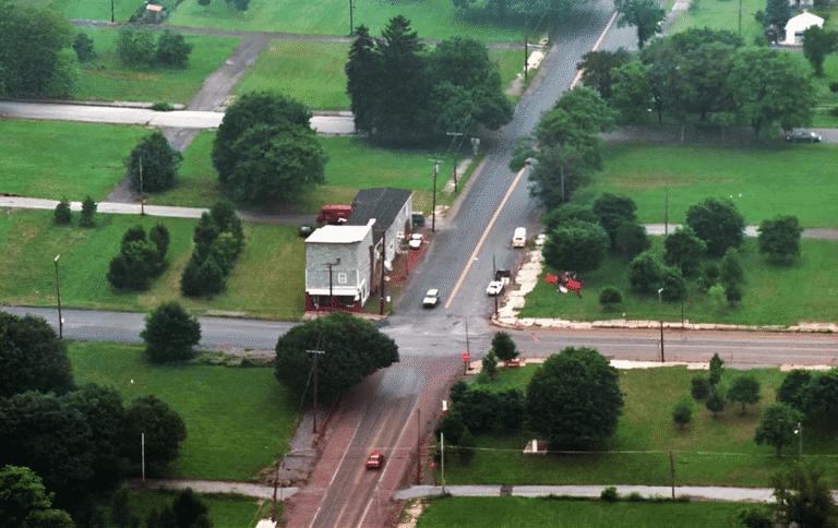 Aerial shot showing a deserted street intersection in Centralia, with sparse buildings and empty roads surrounded by trees and green spaces.