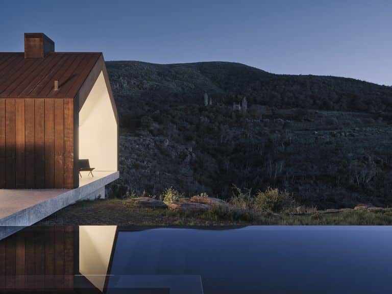 منزل حديث يضم تصميمًا بسيطًا مع سقف مائل وواجهات خشبية، ويظهر في الصورة انعكاسه على سطح الماء في منظر هادئ تحت السماء الليلية