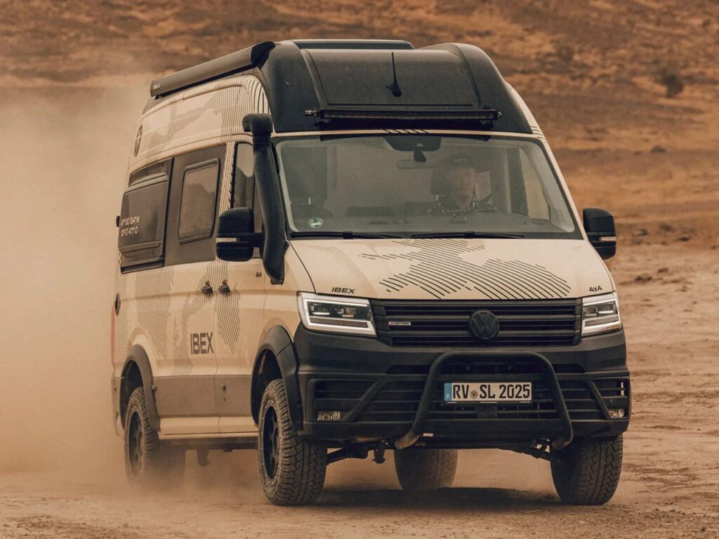 A rugged Volkswagen Ibex Concept camper van drives through a dusty desert landscape, showcasing its durable build and high-clearance design suited for tough terrains.