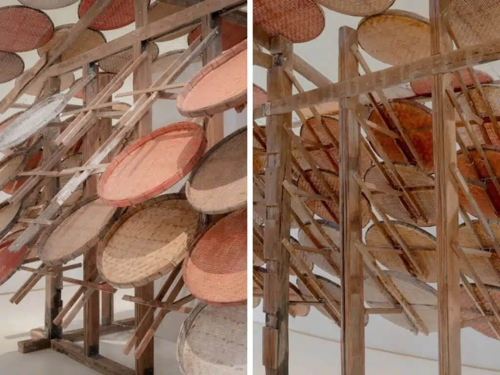 A collection of traditional handcrafted baskets made from natural materials, suspended on a multi-tiered wooden structure. The baskets display natural colors and designs, reflecting local craftsmanship and cultural heritage.