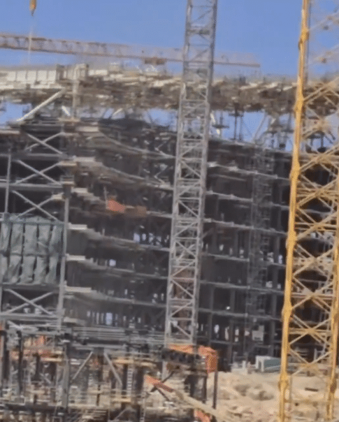 Construction pillars are clearly visible with scaffolding and towering cranes supporting the building process.