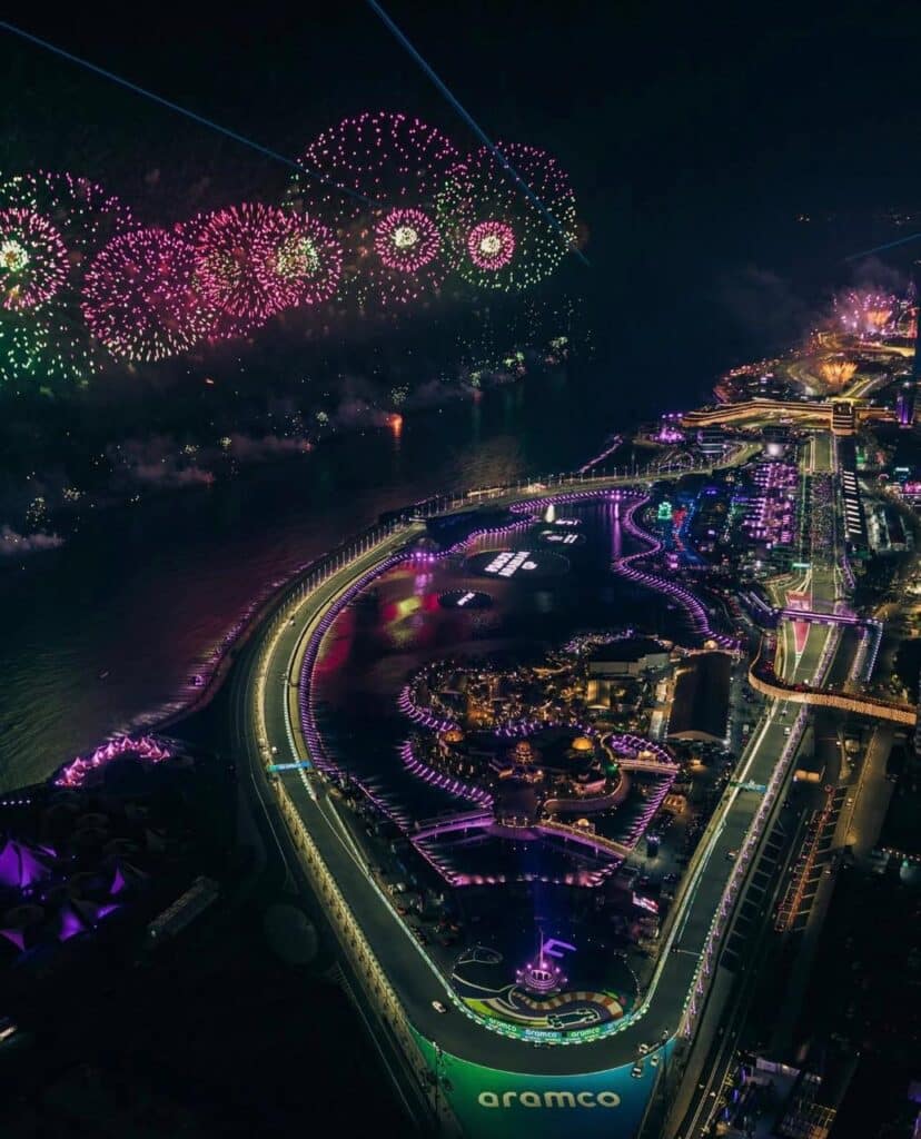 The racetrack lit with vivid lights under a sky filled with colorful fireworks
