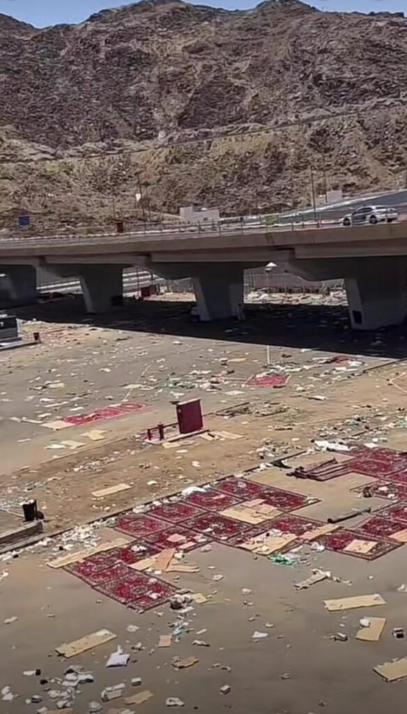 A ground area under a bridge in the Hajj region littered with waste and discarded red carpets.