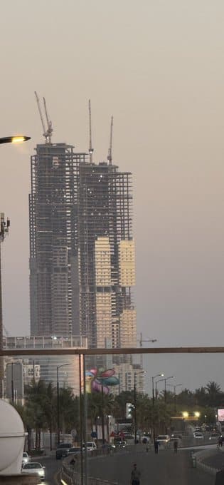 As night falls, the Samo Towers begin to glow from within, with internal and external lighting reflecting off their steel frames. The blend of white and golden light creates a lantern-like effect, as if columns of light are rising into the sky, marking the transition to Jeddah's vibrant nightlife.