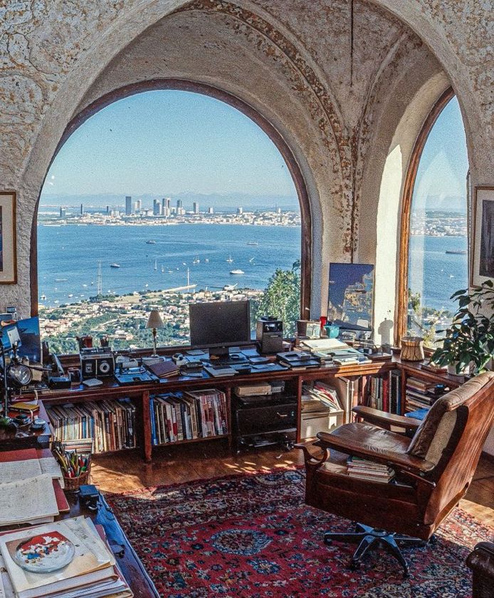 A cozy workspace with large windows offering a stunning view of the sea and surrounding buildings, allowing ample natural light to enter