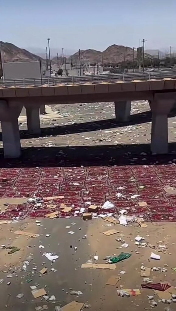 A ground area under a bridge in the Hajj region littered with waste and discarded red carpets.