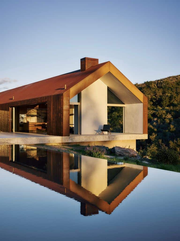 منزل حديث يعكس تصميمًا بسيطًا مع سقف مائل وواجهة خشبية، ويظهر في الصورة انعكاسه على سطح الماء، مما يضفي جمالًا هادئًا