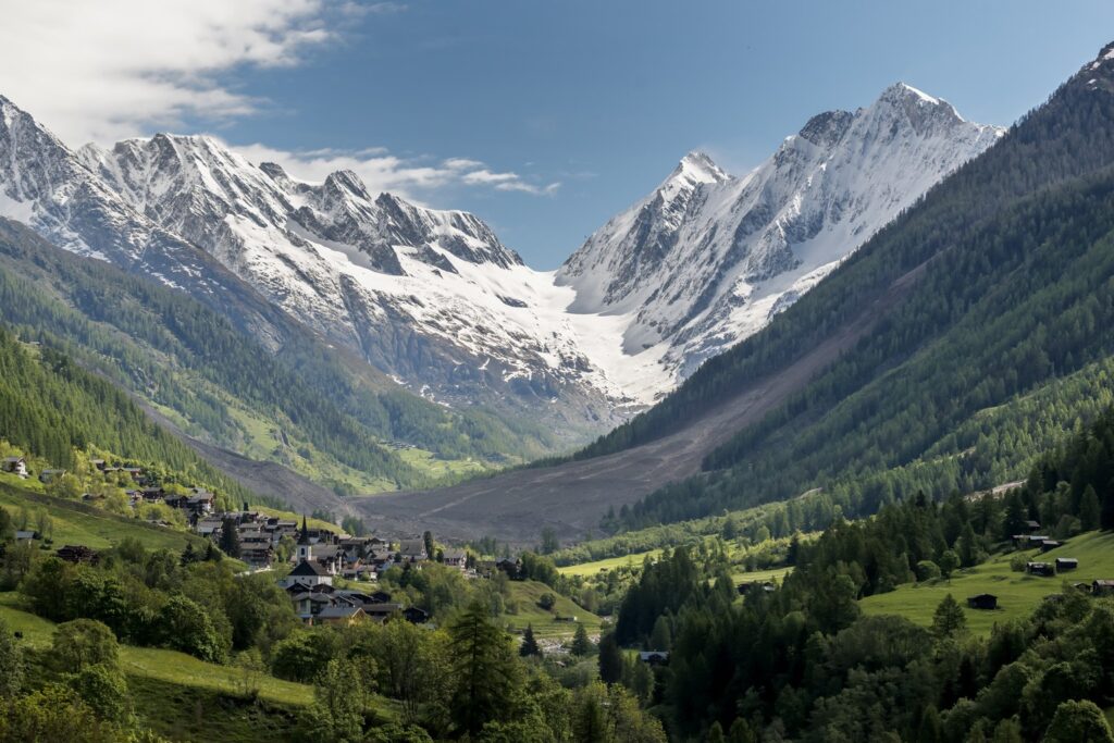 A scenic view of a small village nestled between mountains, with a massive landslide of ice, rocks, and soil descending toward the village due to a glacial collapse.