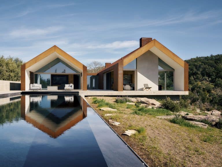 منزل حديث يضم تصميمًا بسيطًا مع سقوف مائلة وواجهات خشبية، ويظهر انعكاسه على سطح الماء في منظر هادئ