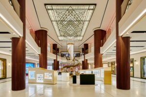 A grand hotel entrance with a stained-glass ceiling, dark wooden columns, and vibrant reception areas featuring bright colors.