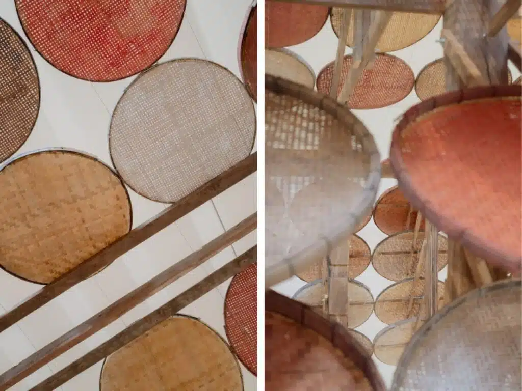 A collection of traditional handcrafted baskets made from natural materials, suspended on a multi-tiered wooden structure. The baskets display natural colors and intricate designs, reflecting high craftsmanship and cultural ties to the local environment.
