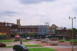 "A historic commercial street featuring a row of old buildings with various shops and small businesses, surrounded by green trees.