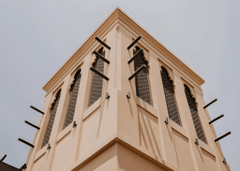 واجهة مبنى تقليدي بألوان ناعمة، تتميز بنوافذ زجاجية مزخرفة وعناصر خشبية سوداء تضيف لمسة جمالية، مع إضاءة طبيعية تبرز التفاصيل المعمارية