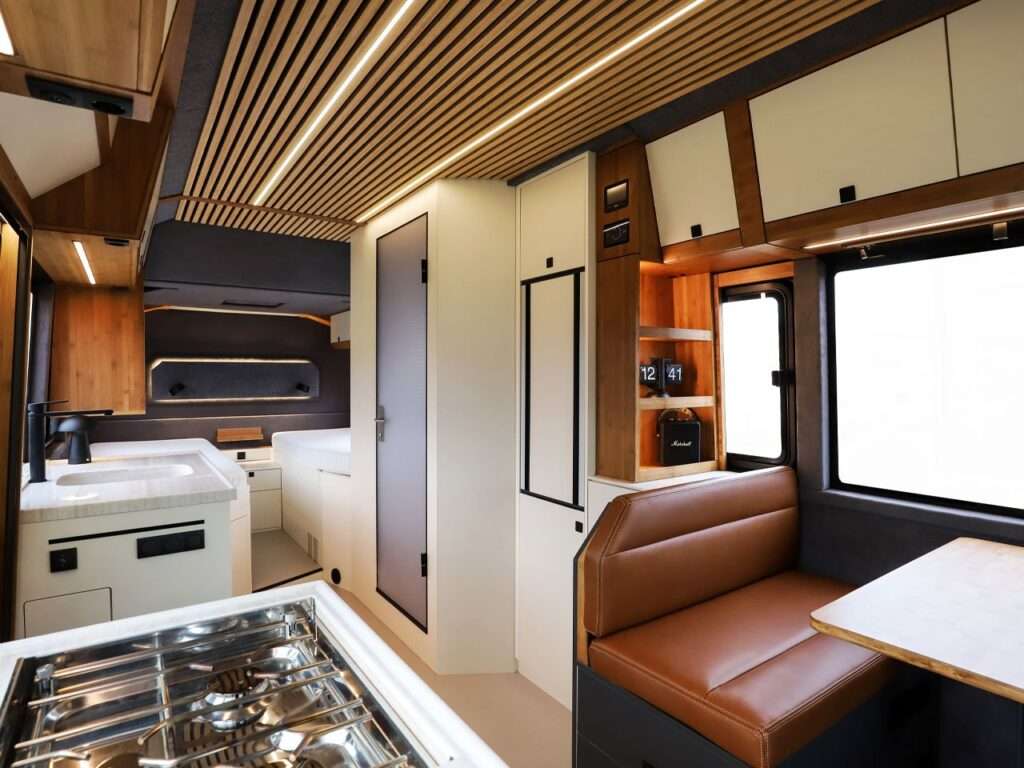 A compact and well-equipped kitchen inside the Torsus Liberra bus, featuring a leather lounge and integrated storage shelves, showcasing a functional yet luxurious design.