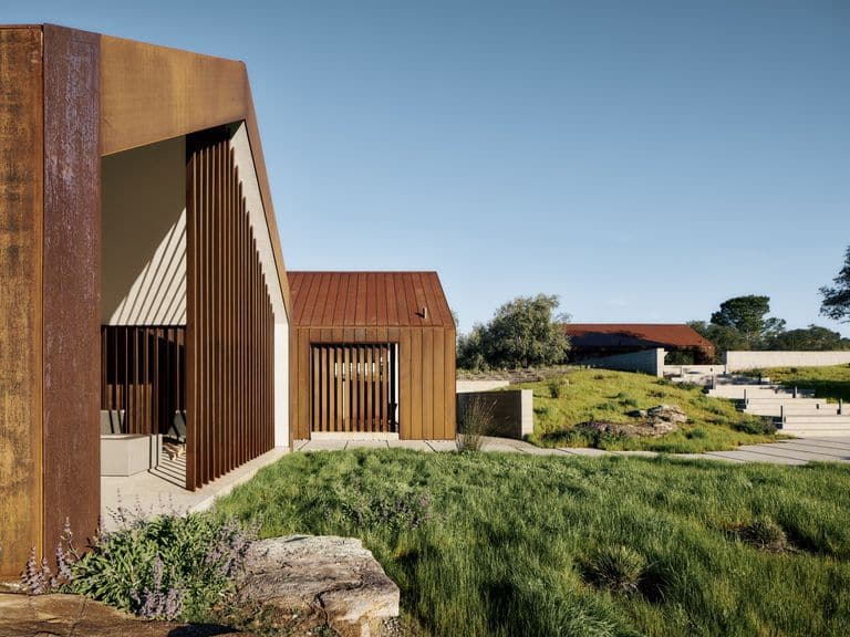 منزل حديث يضم تصميمًا بسيطًا مع واجهات خشبية وألواح فولاذية، ويظهر في الصورة إطلالة على الطبيعة الخضراء المحيطة