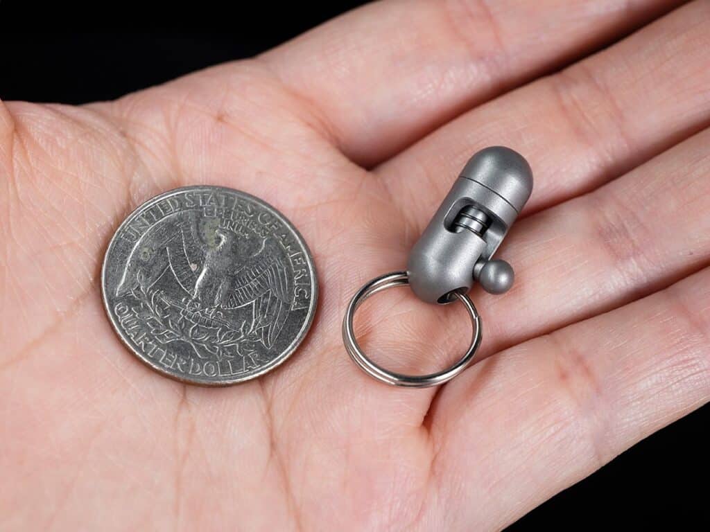 Close-up of a hand holding a compact pocket cutter next to a quarter coin, showcasing its tiny size and portability.