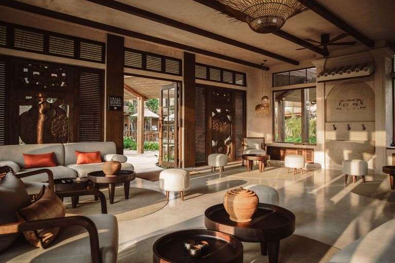 A luxurious living room blending traditional and modern styles, featuring a white sofa with red cushions, small round tables with intricate designs, and wooden furniture that adds warmth to the space.
