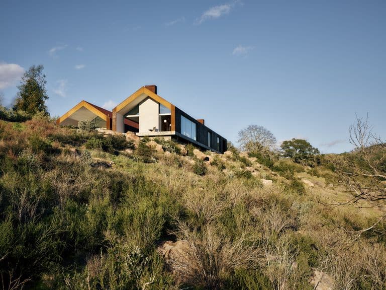 منزل حديث يضم تصميمًا بسيطًا مع سقوف مائلة وواجهات خشبية، ويظهر في الصورة إطلالة على المنحدرات الطبيعية المحيطة