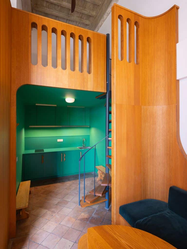 A vibrant and creative small room featuring a wooden staircase leading to an elevated storage or workspace area. Bright green walls and wooden shelves add energy and creativity to the space. The tiled floor brings a traditional touch, while warm lighting enhances the room's beauty.