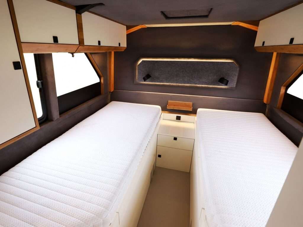 A cozy bedroom inside the Torsus Liberra bus, featuring two neatly arranged beds with warm ambient lighting and side storage shelves, showcasing a functional yet luxurious design