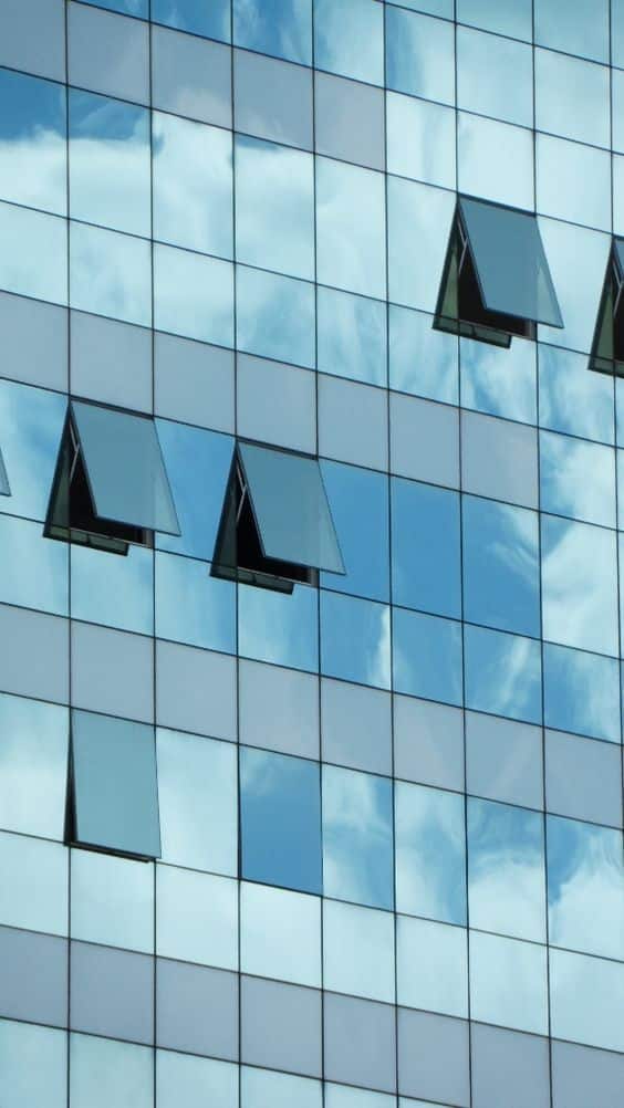 واجهة مبنى حديثة ذات زجاج عاكس تعكس السماء والأبنية المحيطة بطريقة فنية