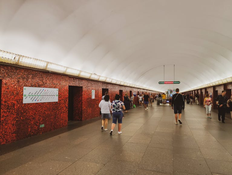 People walking in Moscow's illuminated metro station with red mosaic walls.