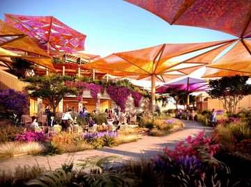 A cozy outdoor area at a luxury resort, featuring a large colorful canopy roof surrounded by vibrant plants. Guests are seated comfortably under the canopies, with flowers and trees creating a serene and inviting atmosphere.