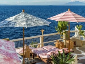 A luxurious seaside lounge area featuring cushioned loungers in vibrant colors under patterned umbrellas, with a direct view of the azure sea.