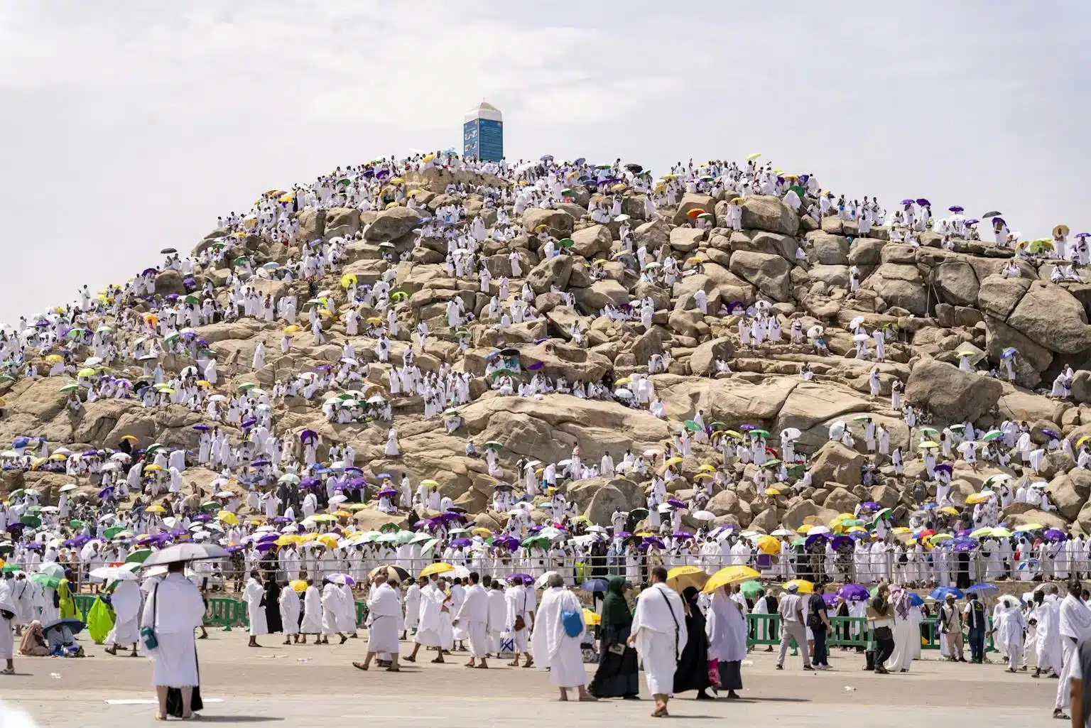 Crowds of pilgrims in white garments holding colorful umbrellas as they gather on Mount Arafat.