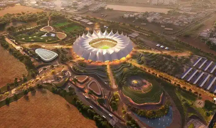 Aerial rendering of a futuristic stadium surrounded by lush greenery and modern infrastructure, showcasing an innovative design with a distinctive dome-like structure.