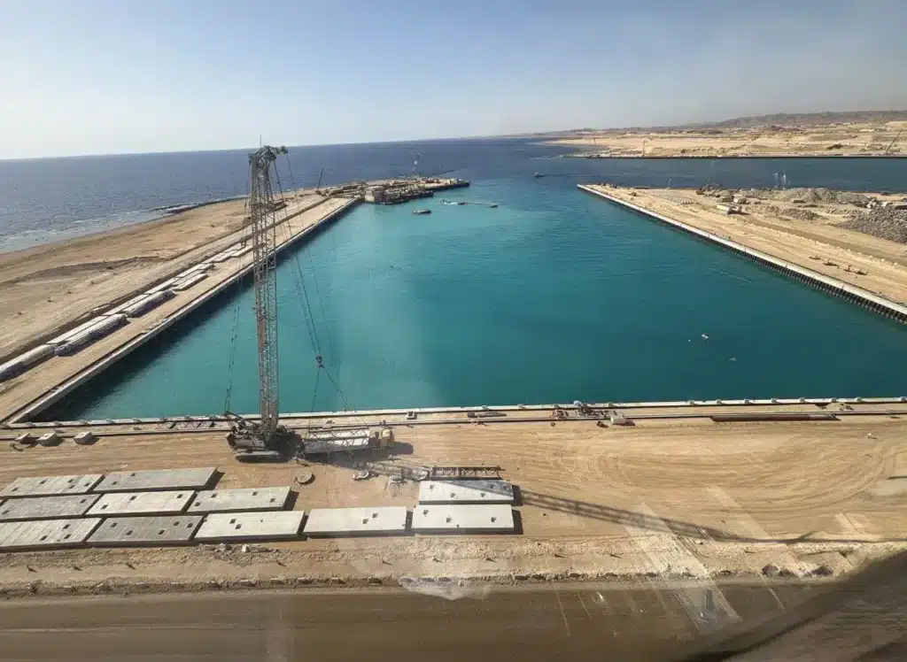 موقع بناء ميناء كبير على ساحل البحر، مع آلة رافعة تعمل على إنشاء قناة مائية