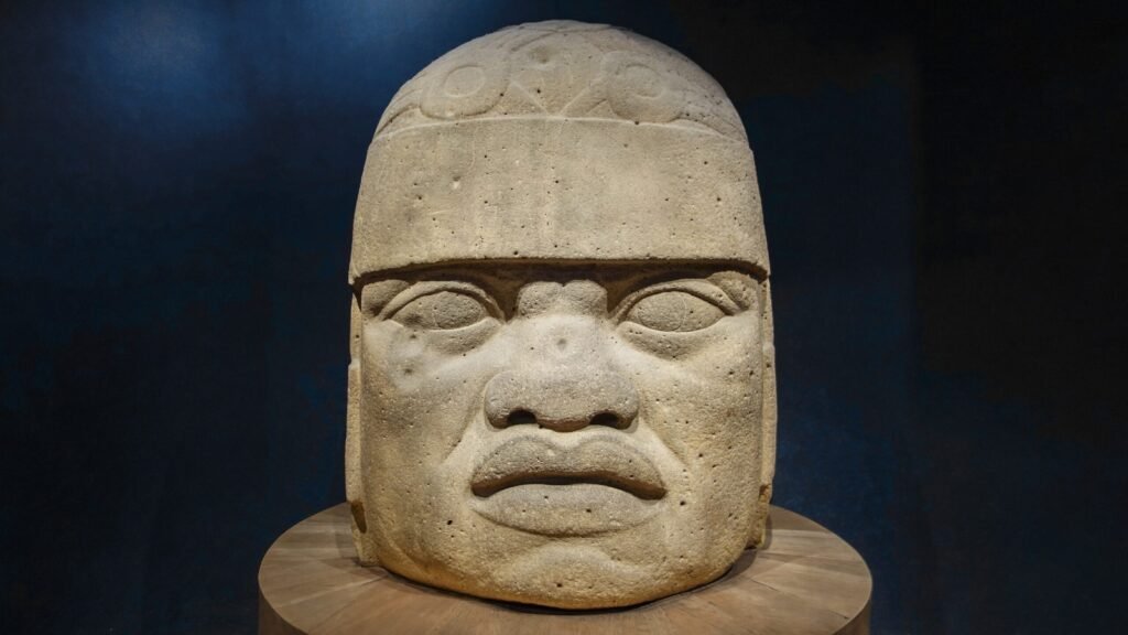 A massive Olmec stone head carved from volcanic rock, featuring strong facial features and fine details, located in Veracruz, Mexico.