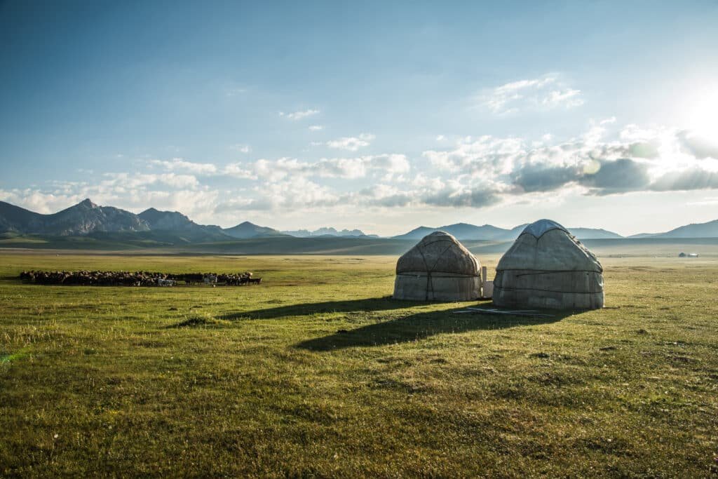 A wide view of a traditional yurt in the Mongolian steppe, surrounded by open landscape and clear skies.