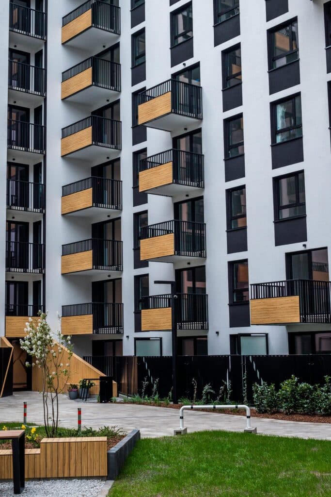 Modern urban residential complex with multiple floors, wooden balconies, and small front gardens.