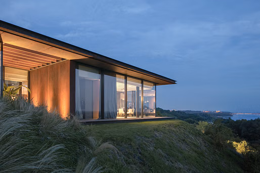 إطلالة مسائية على الواجهة الزجاجية لمنزل "House in the Slope" المدمج في التلة