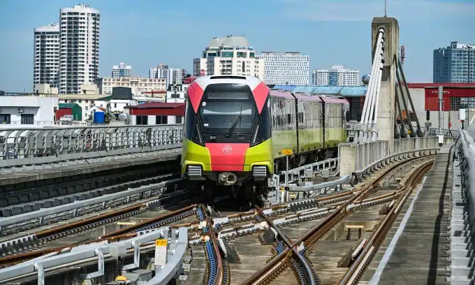 A sleek metro train with vibrant colors travels along an elevated track in an urban setting