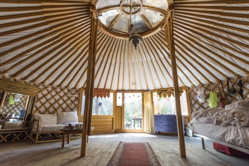 The interior of a yurt showing curved wooden beams and a central roof opening that allows light inside.