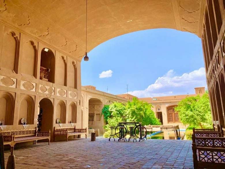ساحة منزلية تقليدية في يزد تحتوي على بركة مياه ونوافذ خشبية، تعكس الطابع المعماري المحلي.