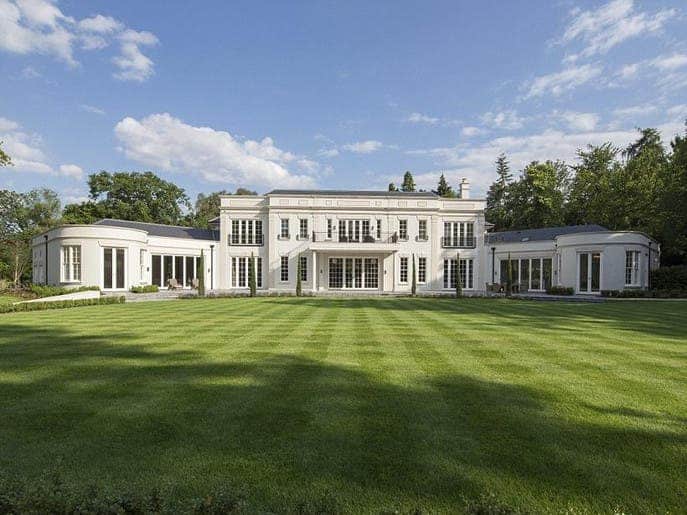 الواجهة الأمامية لقصر كلاسيكي أبيض تحيط به حديقة خضراء واسعة