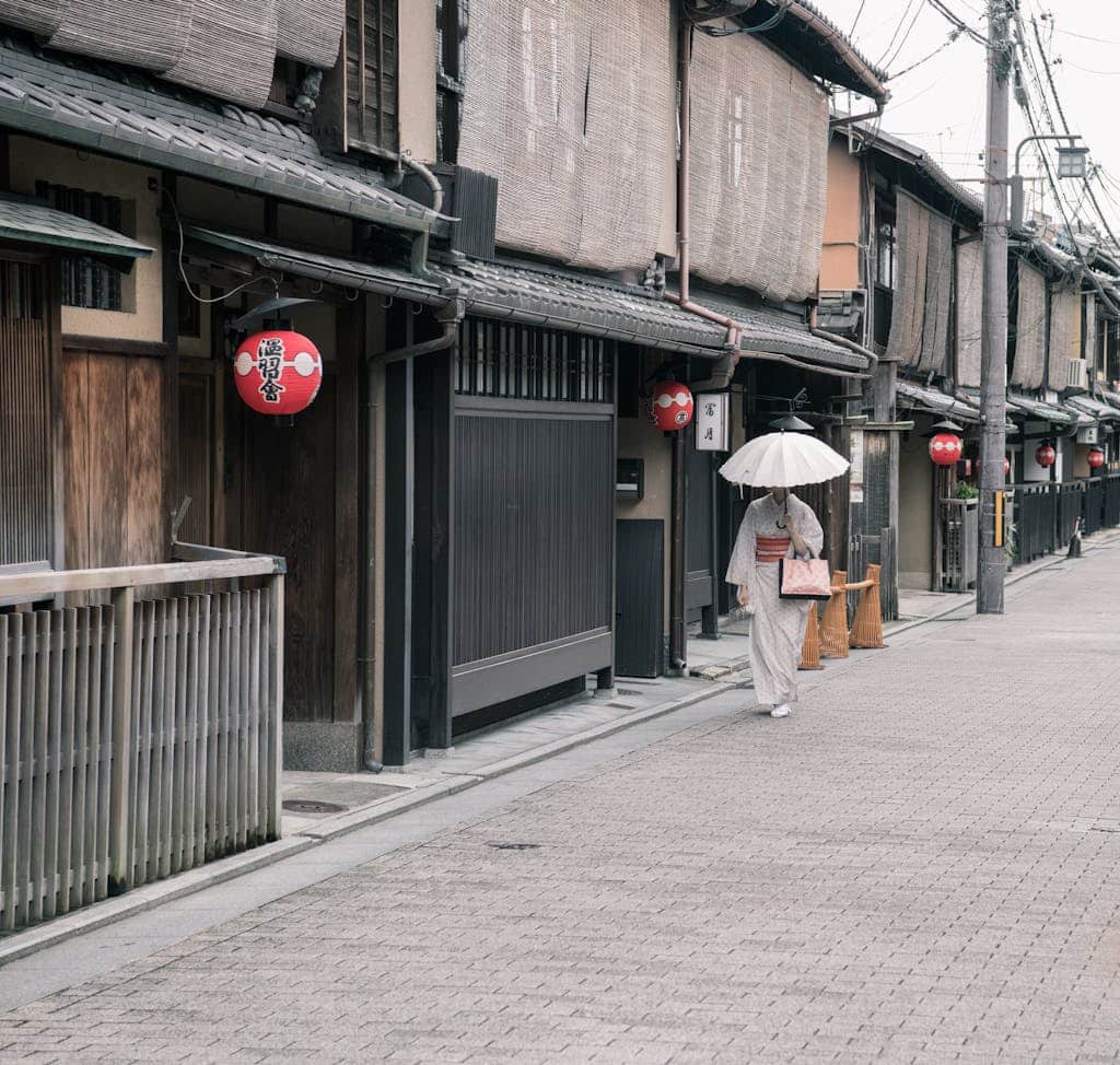 A woman in a kimono walks down a traditional street in Kyoto, Japan, holding an umbrella.