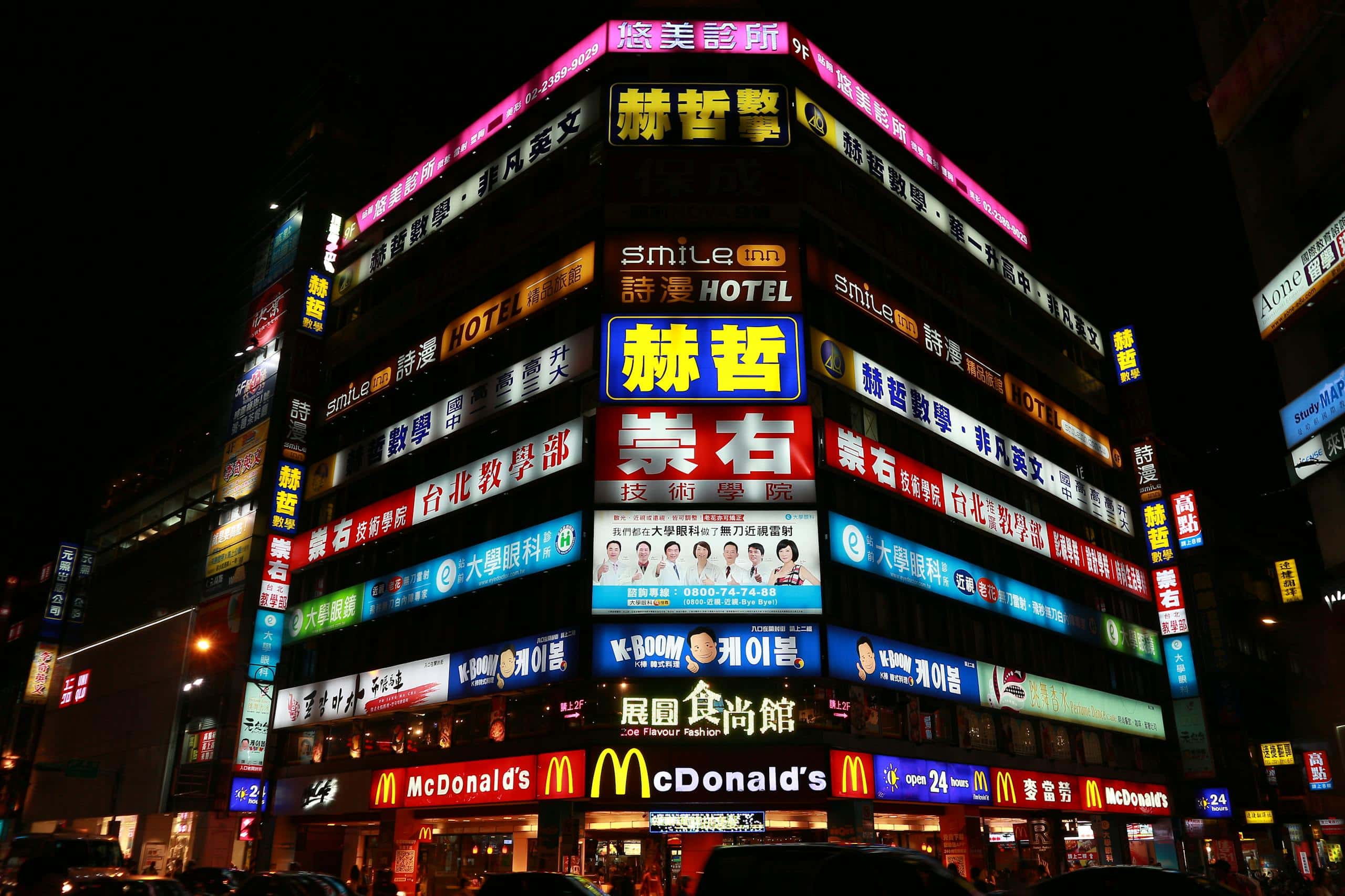 Illuminated building in Taipei showcasing vibrant nightlife and diverse advertising signs on a bustling street.
