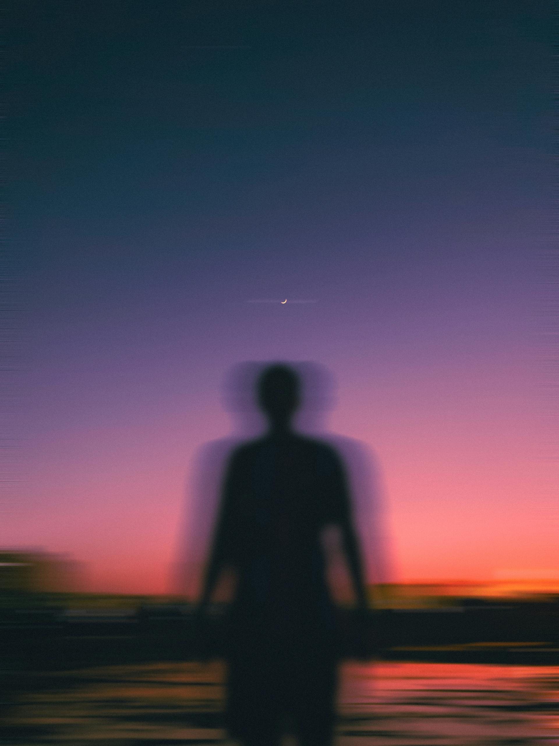 Silhouette of a person against a vibrant dusk sky with a crescent moon.