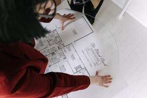 Top view of a woman reviewing detailed architectural blueprints on a glass table, discussing property details.