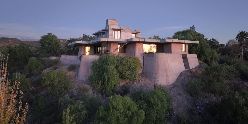 منظر خارجي لمنزل خرساني ضخم مدمج مع الطبيعة على منحدر في مندوزا، الأرجنتين، تظهر الهيكل الصلب بتفاصيل الخرسانة الخام والألوان الترابية.