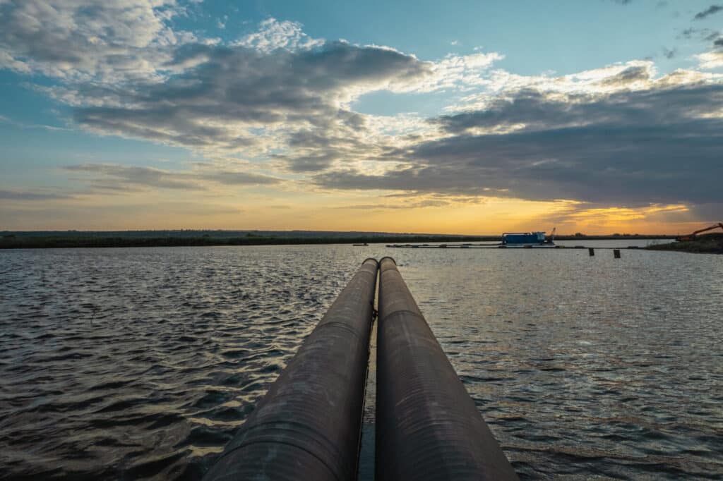 خط أنابيب يمتد في النهر عند الغروب، يظهر تطوير البنية التحتية للمياه في ميكولايف.